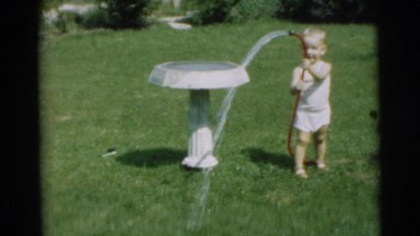 1954: baby girl plays with red hose by a bird bath in a backyard PENNINGTON