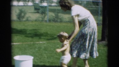 1967: a woman wrestling with her cute child and a bucket in the yard CAMDEN