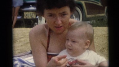 1967: a young woman on the beach with her cute baby bouncing in her lap CAMDEN,