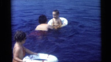 1967: Children Practicing Swimming in Inner Tubes at Lake with Mother