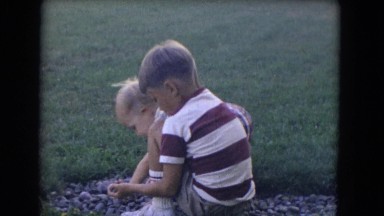 1964: two small children playing side by side with rocks in the yard