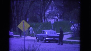 1964: man crosses street on a dark day, children arrive at a building