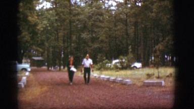 1968: a man and woman walking up the path along a beautiful park with pine trees
