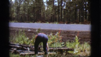 1968: a middle aged man picks up pieces of debris near the side of a road.