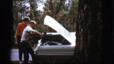 1968: a middle aged man helps young woman by placing firewood in her vehicle's