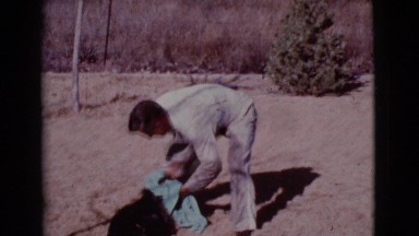 1968: man plays with dog by rubbing it with a blue towel outside COTTONWOOD,