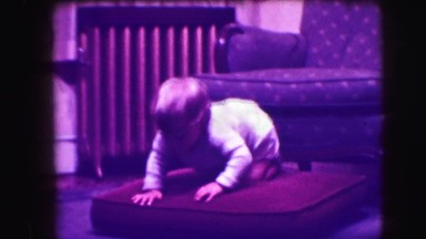 1942: baby in a living room setting crawls down from an armchair, onto a chair
