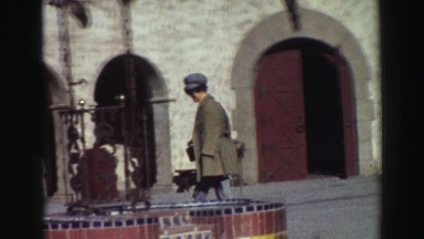 1969: woman walking around a fountain by a stucco building with a bell