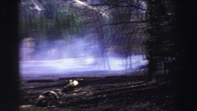 1969: a forest fire along a paved road with a white vehicle driving past.