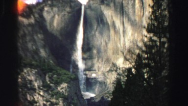 1969: tall waterfall flowing down on sunny day around a thick green forest