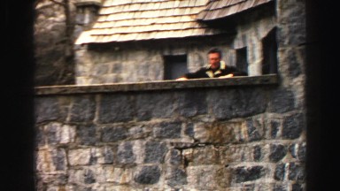 1969: man stands on rock wall after climbing up with bare hands wearing shoes