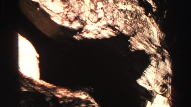 1969: hiker pans rocky cliff dwelling in forest peak into trees and blue skies