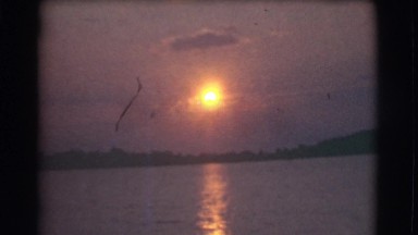1951: the sun glistens orange and is reflected on a lake CANADA