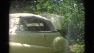 1951: a man unloads the trunk of a cream colored classic automobile