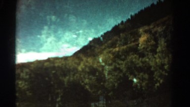 1967: remote mountain lake superimposed over wooded hillside. COLORADO