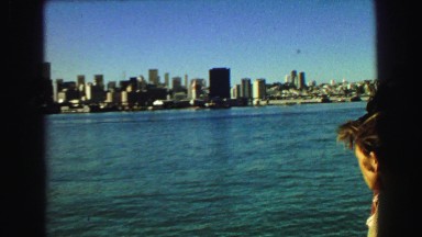 1968: A Boat with a Crowd of People Sailing Near a Coast Full of Buildings