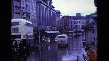 1969: a busy, wet city street with traffic and a double-decker bus ENGLAND