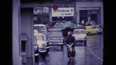 1969: a city urban street wet with rain, featuring a man on a motorbike IRELAND