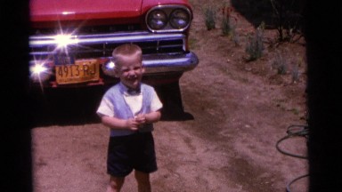 1963: two children laughing while playing in a field against a red wagon CAMDEN