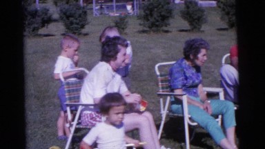 1963: a group of people sitting in a backyard by a sprinkler on a sunny day