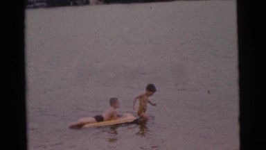 1963: a boy on a raft in the water being pulled by another child CAMDEN
