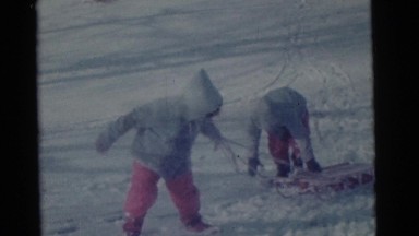 1963: two small children in matching outfits pull a sled on the snow