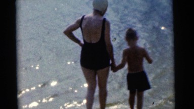 1963: a woman and boy walking into the surf as children play on the beach