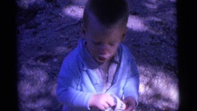1963: toddler with birdie toy, and older child pointing up with fingers outside
