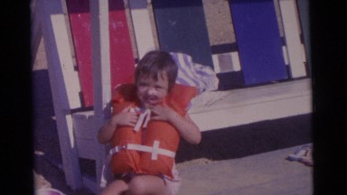 1963: a small child wearing a lifevest on the beach