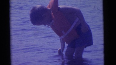 1963: boy walking with life jacket near to playing father and kid CAMDEN
