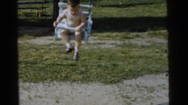 1961: a young boy swinging rapidly on a traditional swing set in the yard