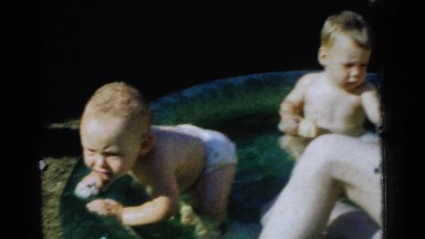 1961: a man plays with two babies in a small swimming pool placed in a yard.