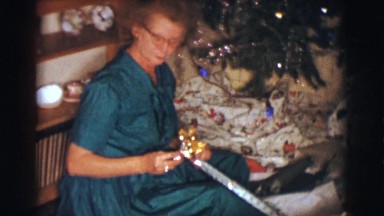 1961: an old lady sits next to a decorated tree and opens a present. CLARKSDALE