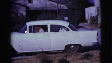 1961: white sedan driving off past a series of houses in a suburban neighborhood