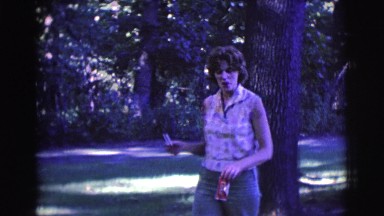 1961: woman walks through wooded area carrying cigarette to give to man.