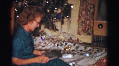 1961: woman opening a gift under the christmas tree. CLARKSDALE, ARIZONA