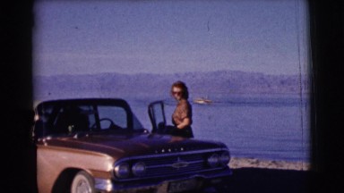 1961: woman blowing kisses beside car at beach CLARKSDALE, ARIZONA