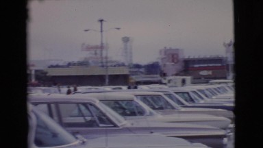 1968: women are walking by a parking lot area full of cars