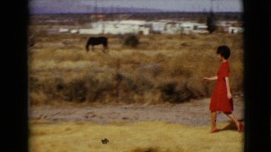 1968: woman in a red dress is walking towards towards a boy on a farm