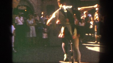 1962: a man on the street in a costume performing on a unicycle