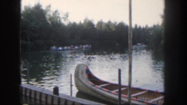 1962: group of people slowly rowing down a river in the woods with calm water.