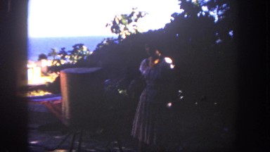 1962: a woman wearing a dress moves in a shaded patio to cook