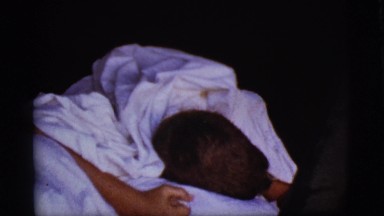 1968: a cute young boy waking up in bed wrapped in white sheets COTTONWOOD