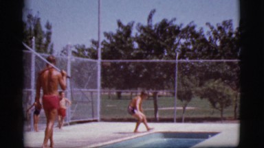 1968: young boy goes swimming while lifeguard walks alongside pool