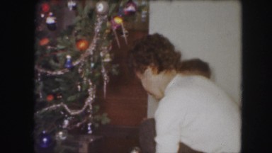 1958: three people decorating a christmas tree in a house in the living room