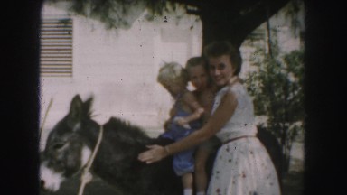 1958: women pets her donkey while her two young children sit on it