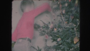 1958: older boy in red shirt and girl in white shirt decorating christmas tree.