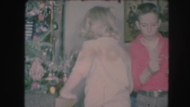 1958: older boy in red shirt and girl in white shirt hanging bulbs on tree.