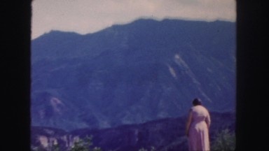 1958: a woman standing alone in a pink dress admiring the beautiful mountain