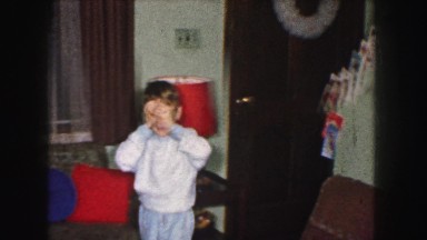 1958: a young boy in pajamas inspecting christmas gifts under the tree